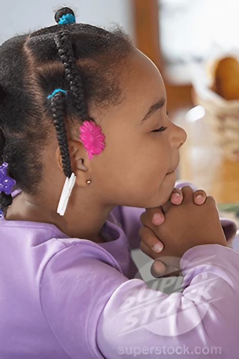 A young girl is praying with her hands folded together.