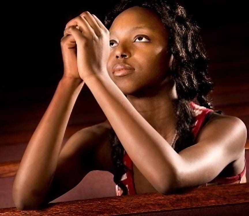 A woman sitting in front of a wall with her hands folded over her face.